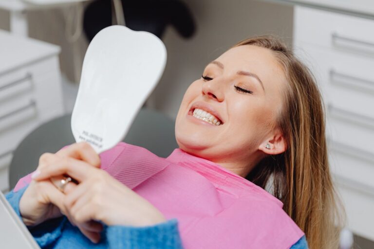 Smiling woman in a dental chair checking her porcelain veneers in a mirror at a clinic in Archway